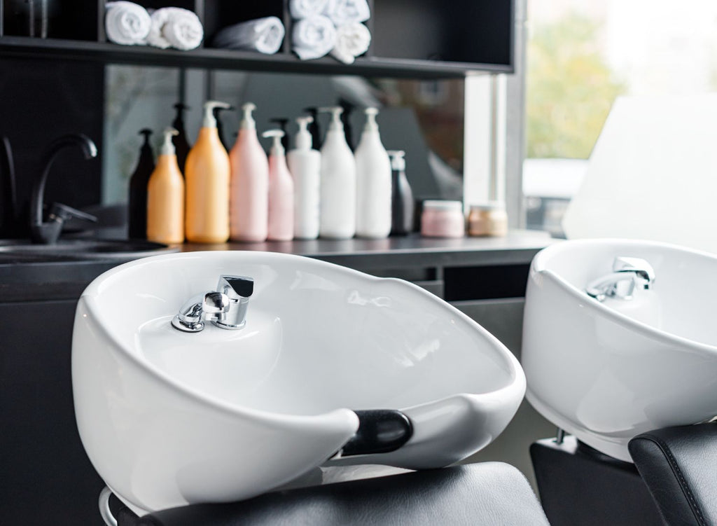 Close up of a sink to wash hair and products on shelves behind it - Operating Costs of Opening a Hair Salon - Lunica Beauty