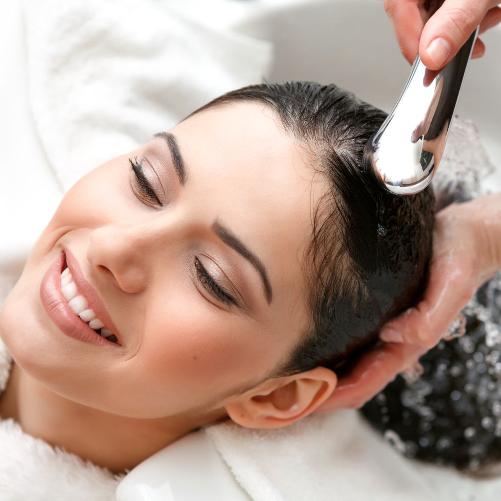 Female clients leans head back into sink as hair dresser washes her hair