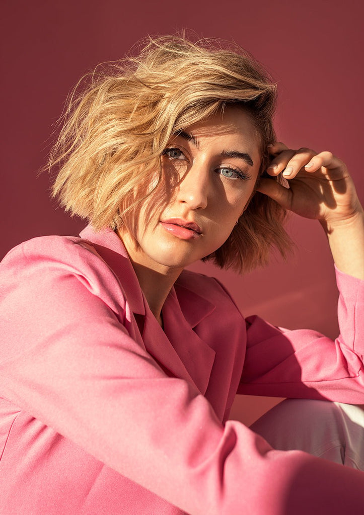 model in pink blazer and a pink background looks at the camera